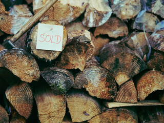 Warm rustic photo of stacked firewood with red SOLD label nailed to a log and a hammer beside it. Soft light, shallow depth, natural wooden texture, symbol of renewable energy and craftsmanship.
