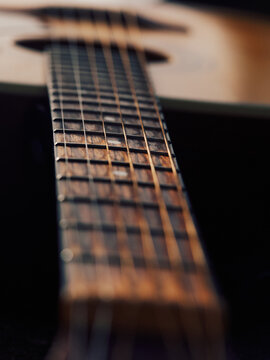 Warm toned guitar shot with soft sunlight, focus on neck in foreground, blurred body in slight tilt in background, subtle shadows at neck, cozy and minimal musical composition, artistic macro feel.