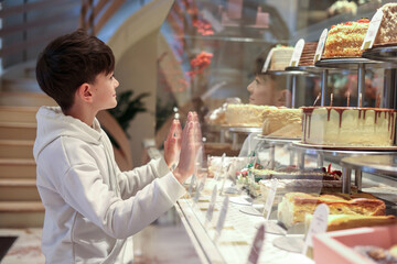 Happy boy admiring cakes in a bakery display, symbolizing childhood joy, sweet treats, and the simple pleasure of desserts.