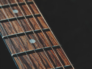 Guitar neck close up, angled from right to left, sharp focus on frets and wood texture, left side dark empty space for text, warm subtle tones, minimalist and artistic macro composition.