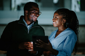 Black coworkers discussing digital content on tablet, smiling