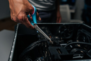 Technician hand cutting network cable inside opened computer tower during precise electronic maintenance and hardware troubleshooting procedure. Concept of desktop PC maintenance and service.