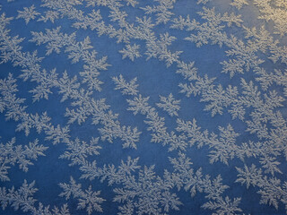 Schneeflocken auf einem tiefblauen Fenster, ein stilles, kristallines Muster, das Reinheit und Ruhe in einem Bild einfängt. Frostiger Morgenhauch taugt die Stille in Kälte.