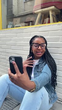 Smiling Latina woman with braided hair Sitting on the street using smartphone