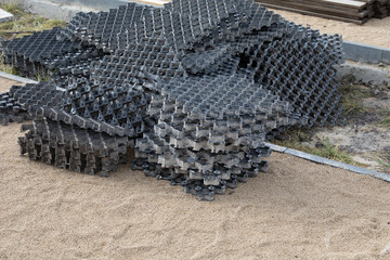 Stacked polymer geogrid panels for soil stabilization on sandy ground. For erosion control, road construction, and permeable pavement systems. Real photo