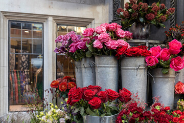 A vibrant outdoor display of fresh flowers for sale, featuring bouquets of deep red and bright pink roses arranged in rustic galvanized metal buckets. © elenarostunova
