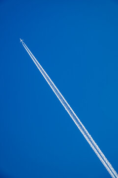 The plane flies, leaving a white trail in the blue sky