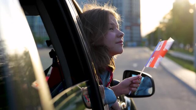 Caucasian little kid girl with Georgian flag in hands looks out of the car window. Cute pretty child travels along Georgian suburbs. Traveling around. Family trip. Close up concept - Powered by Adobe