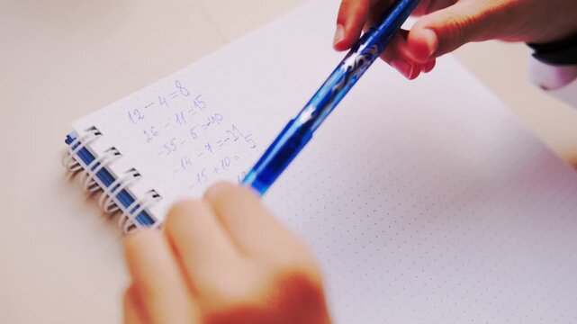 Hand writing math equations in dotted notebook with blue pen, solving arithmetic problems including negative numbers, educational activity, student homework, learning study session, school concept