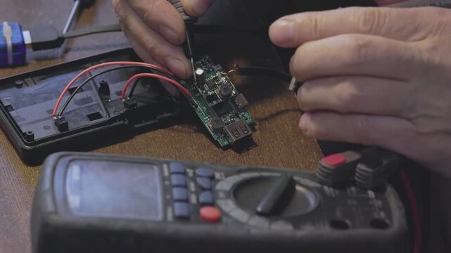 Hands actively engaged in the intricate process of electronic repair using a multimeter and a circuit board