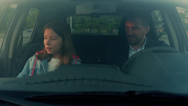 Caucasian teenager sitting in vehicle in front seat. Cheerful Caucasian handsome man waiting in car on little girl. Close up. Dad picks up daughter in car. Family concept. Slow motion