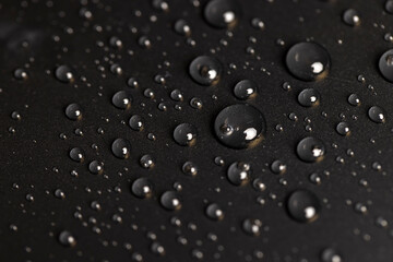 a surface covered with water droplets, details of the wet part of an object made of black plastic