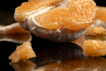 half of an orange citrus on a mirror surface, ripe sweet and juicy citrus is reflected on the black surface