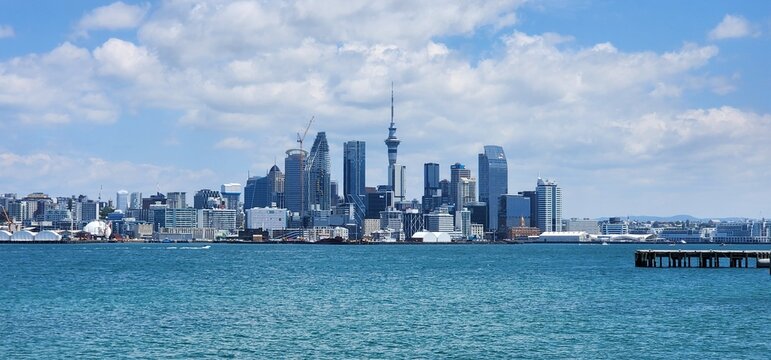 Auckland, New Zealand - 18 January 2025: Daytime View of Auckland Skyline and Sky Tower from Waterfront. Calm blue water in the foreground and a partly cloudy sky enhance the coastal atmosphere.