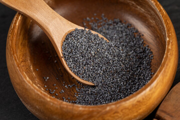poppy seeds poured into a wooden bowl used in the manufacture of confectionery, a large amount of poppy seeds in a wooden bowl with a spoon