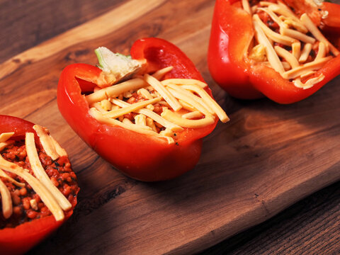Fine red stuffed red peppers with rice, herbs and cheese on wooden cutting board. Premium high quality food with tasty ingredients. Cooking fancy dish.