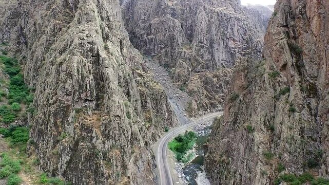 Aerial drone view of a high rocky mountain highway passage in an Asian valley. The road cuts through a narrow, deep canyon between high elevation rocky ridges.