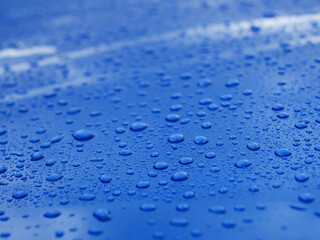 The image is of a blue surface with many small drops of water on it. The drops are scattered all over the surface, creating a sense of movement and energy. Background for design with rich color