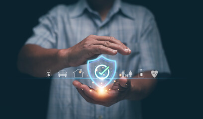 Insurance and protection concept. Businessman holding holographic shield with icons of health, family, house and car. Symbolizing safety, financial security, life coverage and risk management