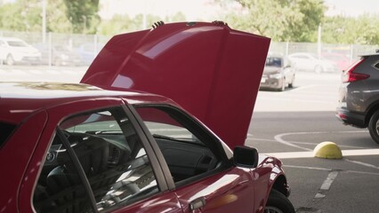 Happy young male driver closing car hood on the parking in the city.