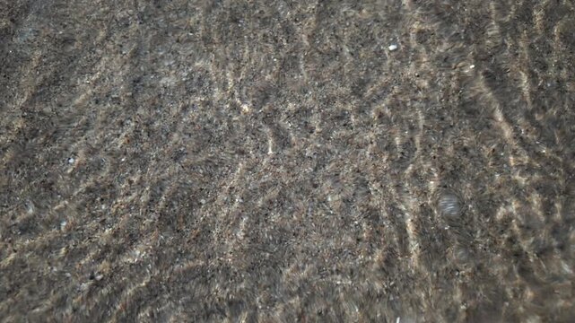 Calm underwater view showing sand ripples and light reflections beneath the sea surface