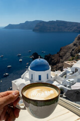 Deliciosa y cremosa taza de café y detrás el paisaje de la isla de Santorini y el mar azul. Felicidad y alegría de viajar. 