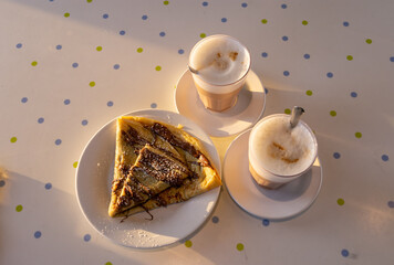 Crep con dulce con dulce de leche o crema de avellanas y dos vasos de capuchino. Vista desde arriba, luz de la tarde.
