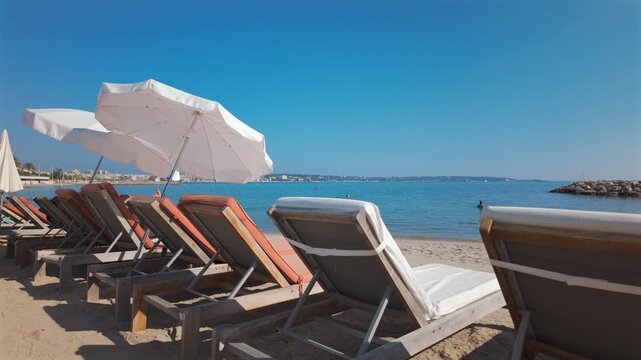 Row of empty sun loungers with white umbrellas on a sandy beach by the calm blue sea