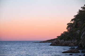 Tranquil sunset over Alacasu Paradise Bay (Cennet Koyu) near Kemer, Turkey. Warm pastel sky above the calm Mediterranean Sea and rocky coastline.