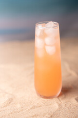 refreshing tropical drink with ice in a tall glass on sandy beach background evoking a calm and serene summer atmosphere with soft blurred horizon, bliss, minimalistic, daylight, relaxing, hydrating
