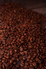 close-up view of rich, freshly roasted coffee beans scattered across a wooden surface, highlighting their glossy texture, deep brown color, and natural rustic atmosphere, aromatic, essence, gourmet
