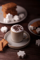 cozy coffee arrangement with a frothy drink topped with chocolate sprinkles and surrounded by gingerbread cookies and snowflake-shaped marshmallows on a rustic wooden surface, toppings, leisure