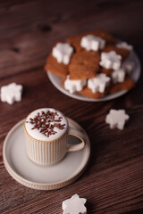 cozy warm setting featuring a cup of foamy coffee adorned with chocolate sprinkles and festive gingerbread cookies with white star-shaped marshmallows on rustic wooden table, casual, background