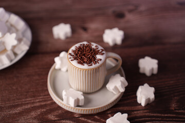 warm coffee in a ribbed cup topped with chocolate sprinkles surrounded by white marshmallow snowflakes on a wooden table, creating a cozy winter ambiance with soft lighting, serene, calm, indoors