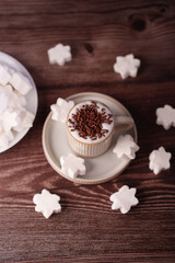 a cozy arrangement features a cup of creamy cappuccino crowned with chocolate sprinkles, surrounded by snowflake-shaped marshmallows on a rich wooden surface evoking warmth, art, culinary