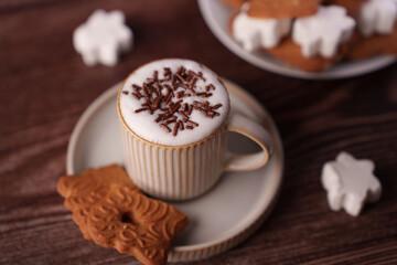 warm cozy scene featuring a cup of frothy coffee topped with chocolate sprinkles and accompanied by gingerbread biscuits and marshmallows set on a wooden table highlighting festive ambiance, festive