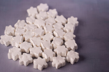a multitude of white, star-shaped marshmallows are scattered on a textured gray surface, creating a soft contrast and evoking a playful and cozy atmosphere, serene, display, array, composition