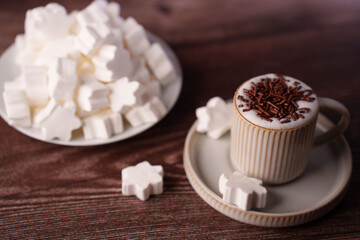 close-up of fluffy hot chocolate topped with chocolate sprinkles and surrounded by white snowflake marshmallows on a wooden table setting, stylish, aromatic, delicious, mocha, rustic, comforting