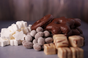 assorted winter-themed sweets featuring white marshmallows, chocolate-covered gingerbread, sugar-dusted almonds, and fudge on a textured gray and brown background, arrangement, decadent, variety