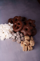 assorted chocolate and marshmallow treats arranged on a textured surface, featuring dark chocolate-covered pretzels, white marshmallow stars, powdered chocolate almonds, and striped white chocolate cu