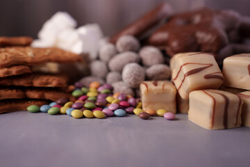 assorted confectionery delight featuring colorful candy, white chocolate squares, biscuits, and sugary marshmallows in a cozy, tempting arrangement on a neutral background, confections, pleasing