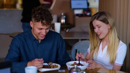 Close up of happy young girlfriend smiling and feeding her boyfriend indoors. Slow motion. Caucasian cheerful couple sitting in restaurant eating on a romantic date. Love concept