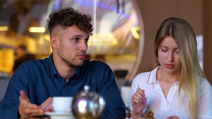 Caucasian young handsome serious man speaking with pretty woman while sitting in restaurant. Boyfriend and girlfriend together in cafeteria in bad mood. Close up shot. Couple on a date