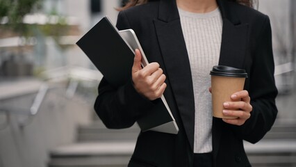 Young businesswoman walking downstairs in offices aria with tall contemporary buildings. Close-up,...