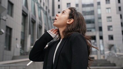 Fototapeta premium Young Caucasian female with dark long hair walking in city center around grey skyscrapers, girl likes view of high contemporary architecture.