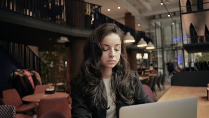 Close up, slow motion. Caucasian Businesswoman working remotely, inside of cafe. Girl look at the window, thinking and looks serious