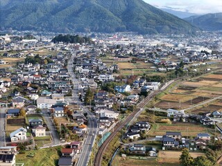 The city is full of houses and a train track runs through the middle of it. The train track is surrounded by a green area and there are many cars on the road. The city has a mix of residential