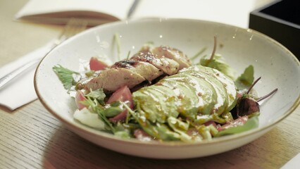 Young woman eating healthy salad with avocado and chicken meat while sitting on the table in cafe. Close up. Healthy food, keto diet concept. Slow motion