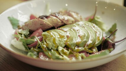 Salad mix with avocado and chicken meat with balsamic dressing on a white plate. Close up. Healthy food, keto diet concept. Slow motion