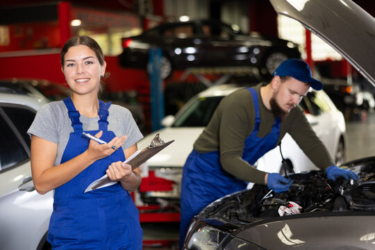 Smiling female worker of auto service welcoming clients holding sheets of paper ready to take notes - Powered by Adobe